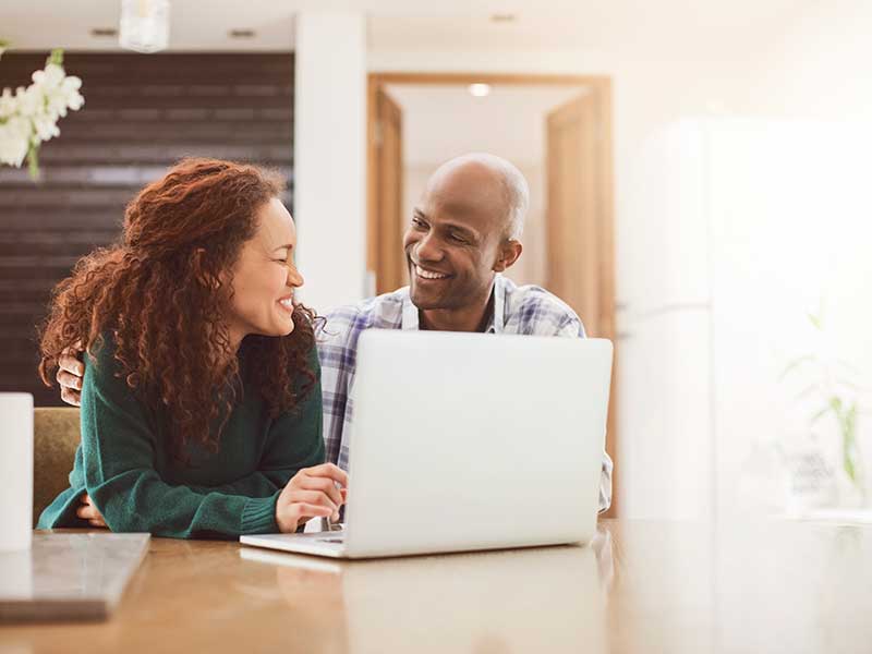 A man and a woman looking at a laptop together and smiling.
